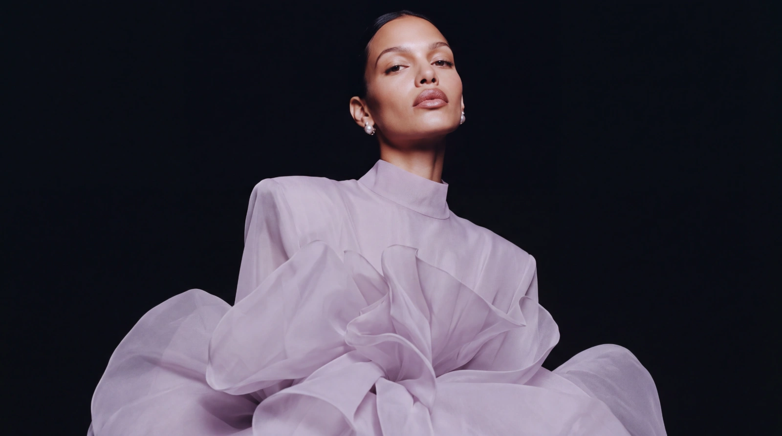 Model in a sculptural lilac organza couture look, photographed against black